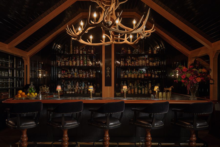 auric room social members club western speakeasy saloon with moody dark wallcoverings antler light suspended above bar